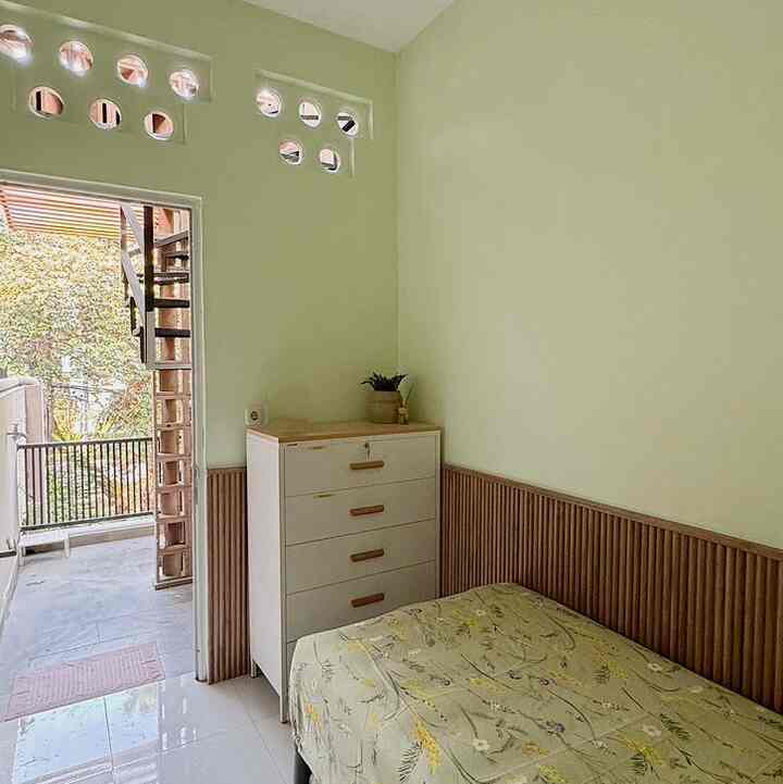 Narrow bedroom with pale green walls and wood-tone paneling, furnished with a white chest of drawers, creating a cozy and clean space