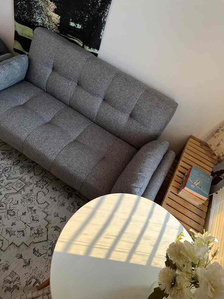 Gray and white toned living room featuring a two-seater sofa, round table, and wooden shelf creating a cozy space