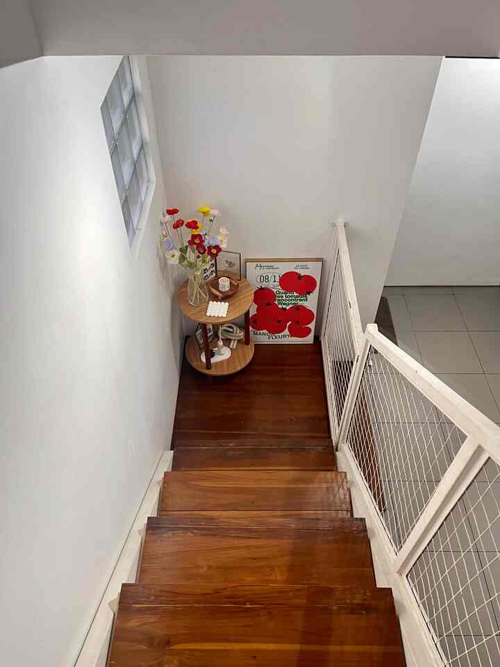 Bright corner space with white walls and wood-tone stairs featuring a vase with flowers and wall decor, creating a cozy atmosphere