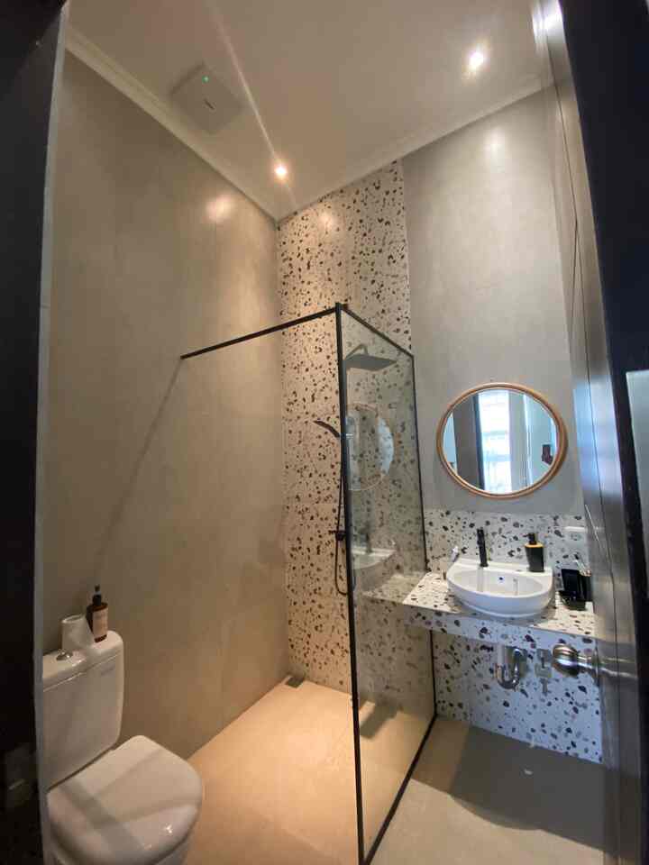 Beige and gray toned bathroom featuring black terrazzo tiled wall, shower booth with black frame, round mirror, and sink in a modern setting