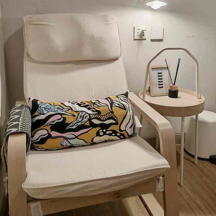 A cozy bedroom corner with white and wood tones featuring iconic IKEA armchair and colorful cushion
