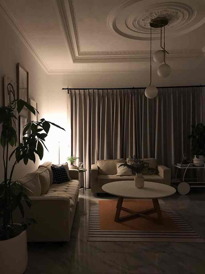 Light beige toned living room featuring two sofas, a round coffee table, pendant lighting, and plants creating a cozy atmosphere