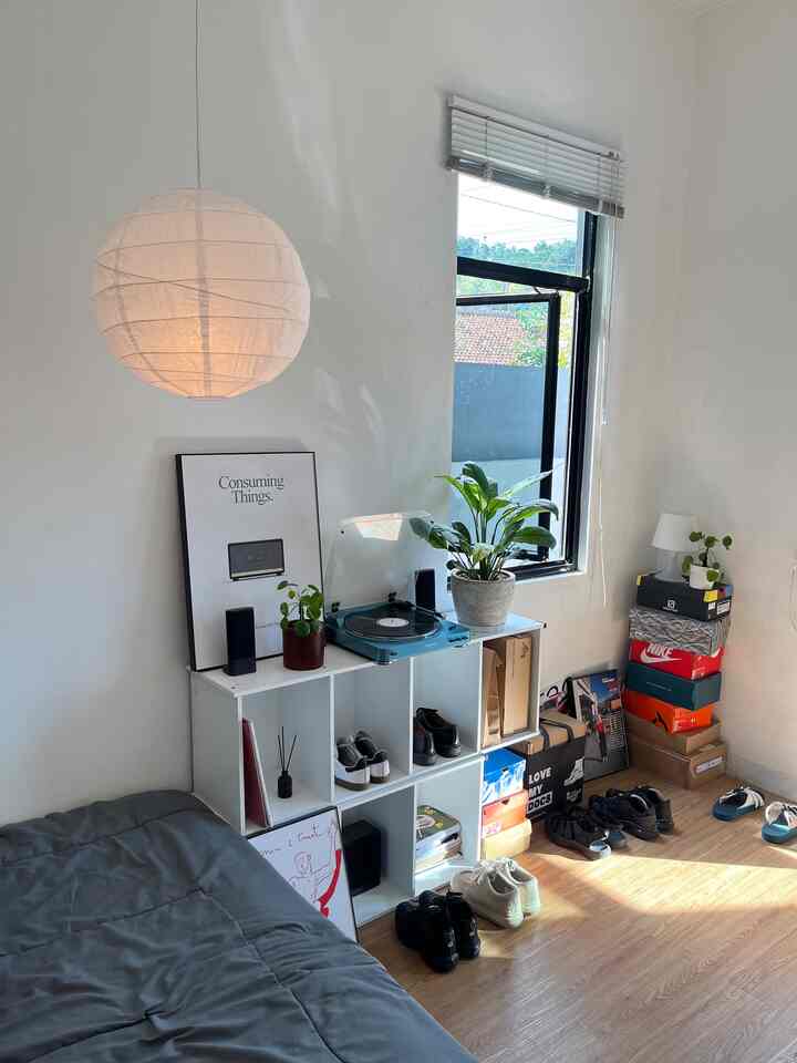 Minimal bedroom with white walls, wood tone flooring, plants, and poster arranged in a compact single household space