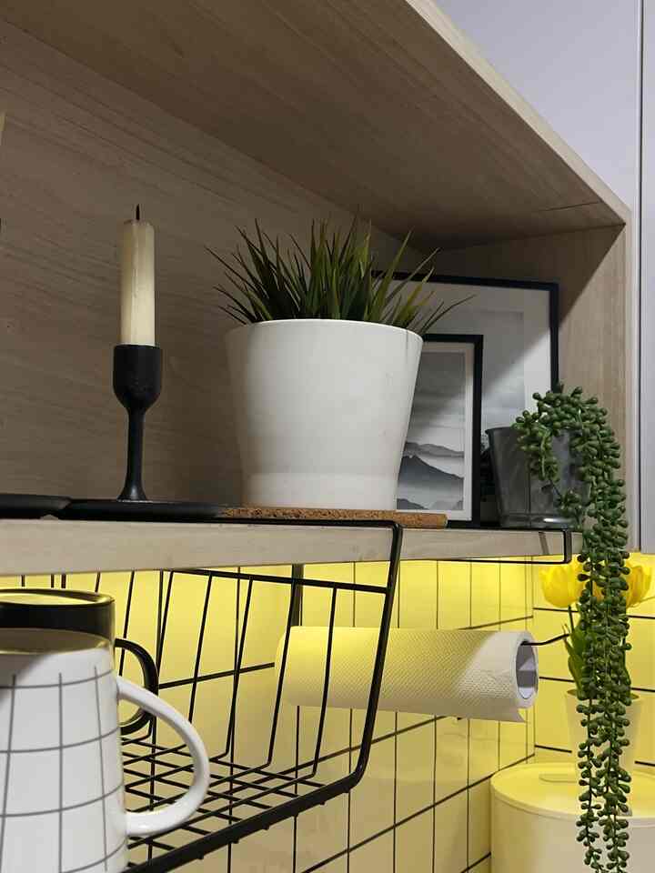 Yellow tiled kitchen wall with white potted plant and black candle holder on shelf