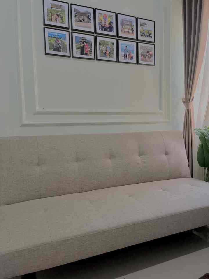 Beige sofa bed in a clean living room with framed photos on the wall and curtains
