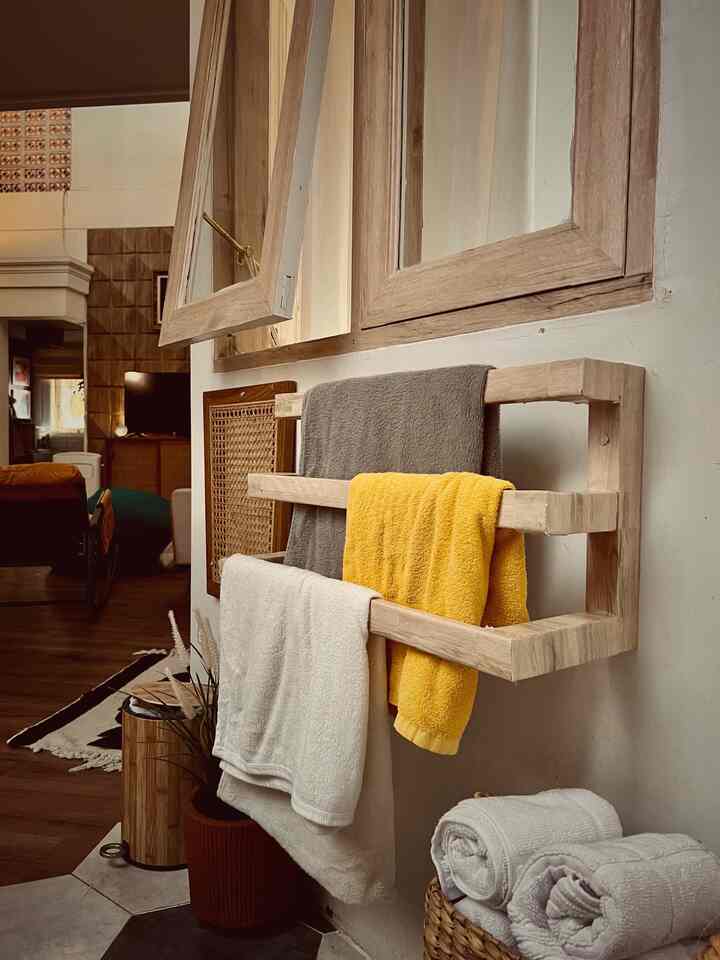 Warm bathroom space with vintage wood tones and beige walls featuring a wooden towel rack holding towels in various colors