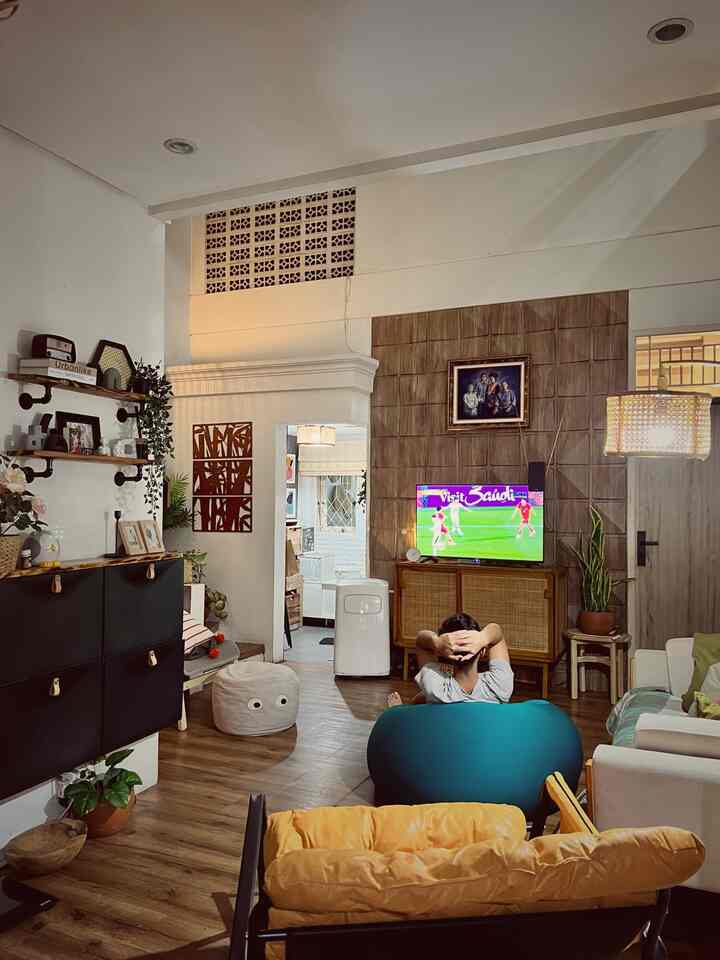 Cozy living room with wood tones featuring orange armchair and turquoise bean bag, person watching TV