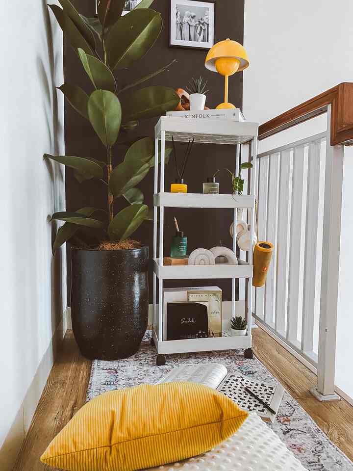 White-walled stair corner featuring a white storage rack, wood-toned floor, yellow cushion and lamp accentuating a cozy Boho style