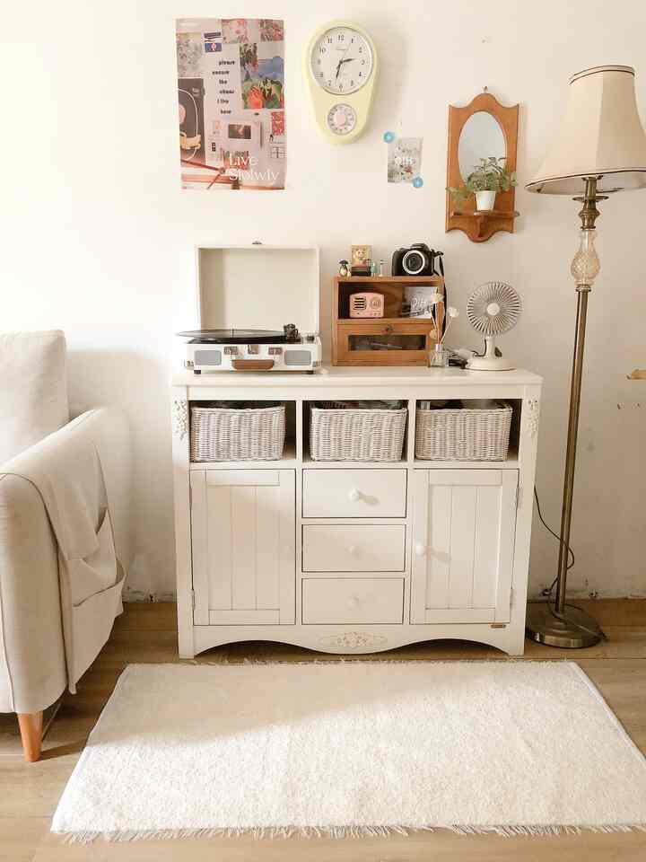 Bright white and wood tone living room featuring a vintage cabinet, sofa armrest, and floor lamp with a warm atmosphere