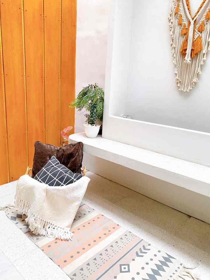 Bright white and warm orange toned serene veranda featuring a patterned rug and cushions in a natural resting area