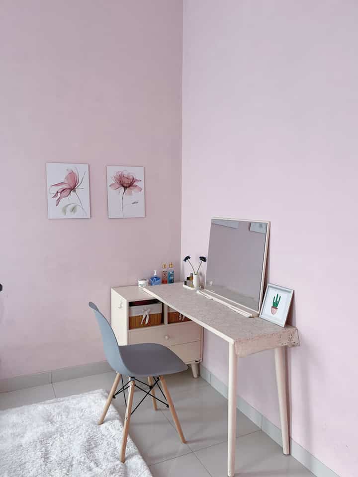 Cozy powder room with pastel pink walls and white flooring, featuring a simple vanity desk and gray chair