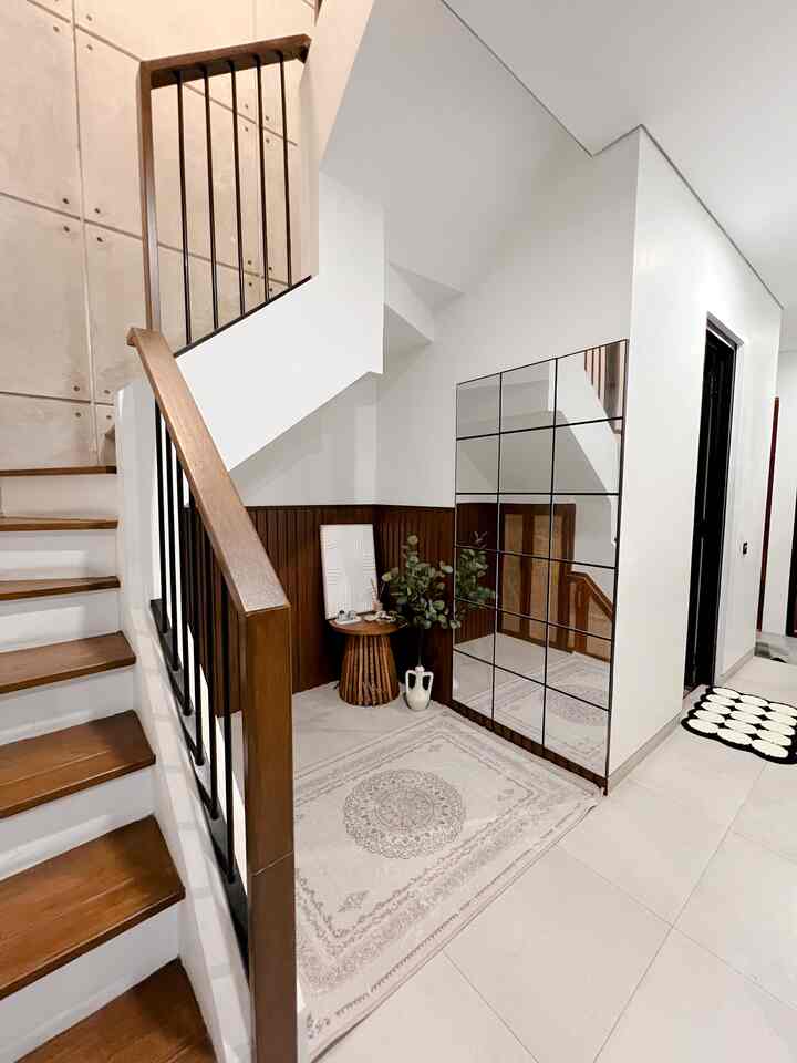 White and wood tone entrance area beside stairs featuring large mirrors, rug, and wall decor for a cozy interior
