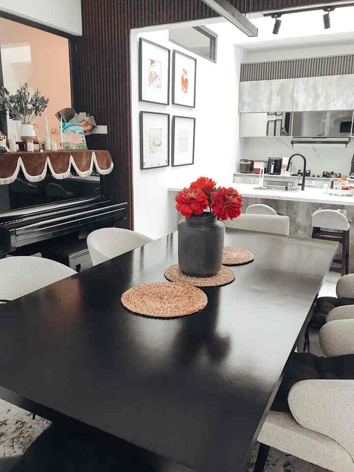 Modern dining room with a black table and beige chairs, featuring a gray vase with red flowers and woven placemats