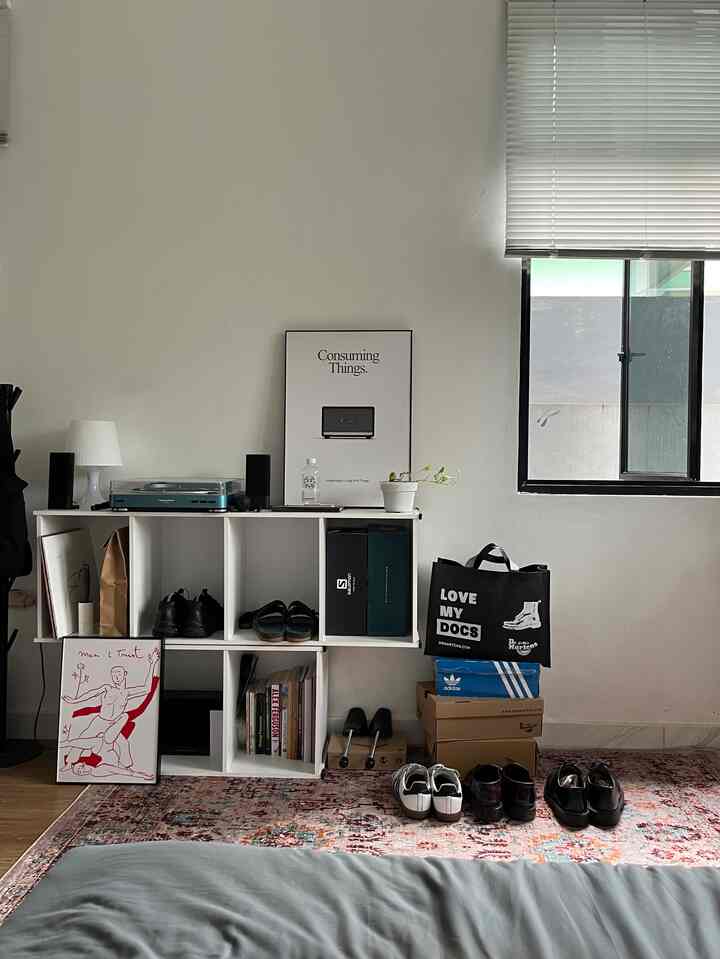 White walls and brown wood-tone floor in a compact studio featuring bookshelves with shoes and storage boxes