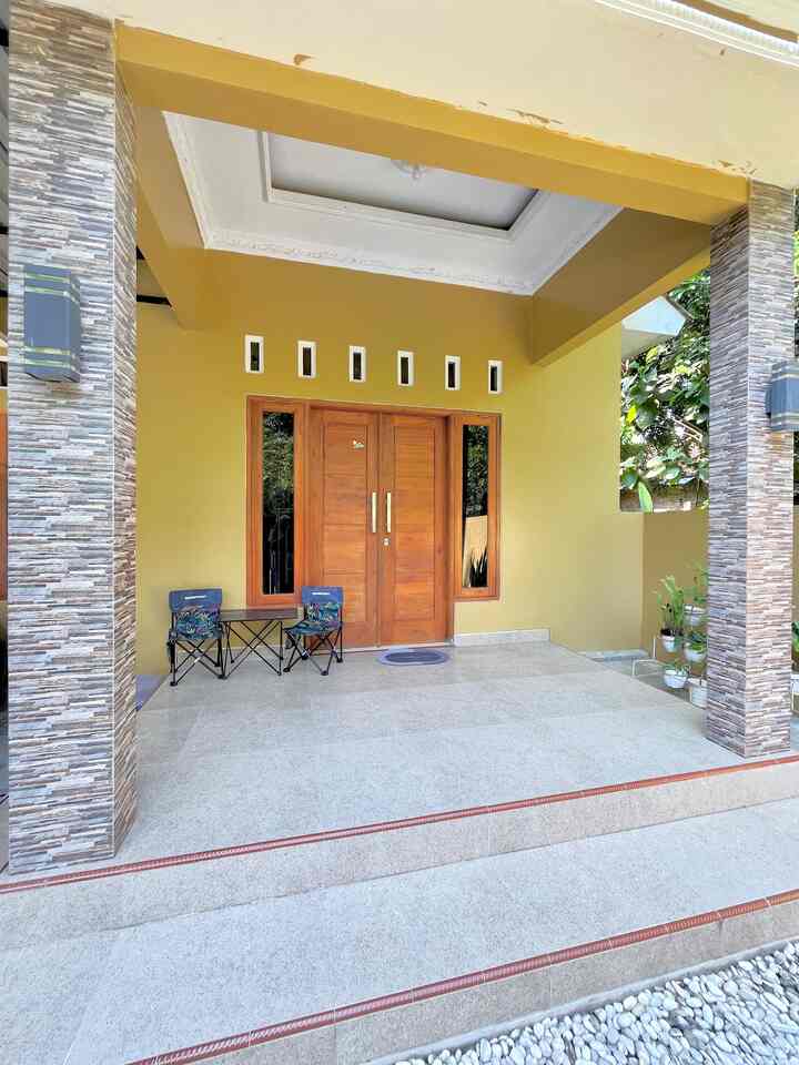 Yellow-walled porch with wood-tone entrance door, featuring 2 foldable outdoor chairs and a small table creating a cozy outdoor entrance