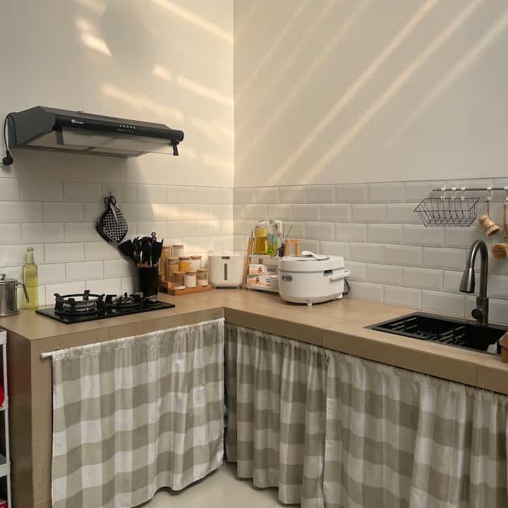 Compact kitchen in white and wood tones, bathed in natural light from a skylight, featuring minimalist storage with curtains