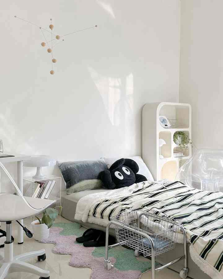 White-walled compact bedroom with green accents, featuring simple furniture and a low bed in a cozy setting