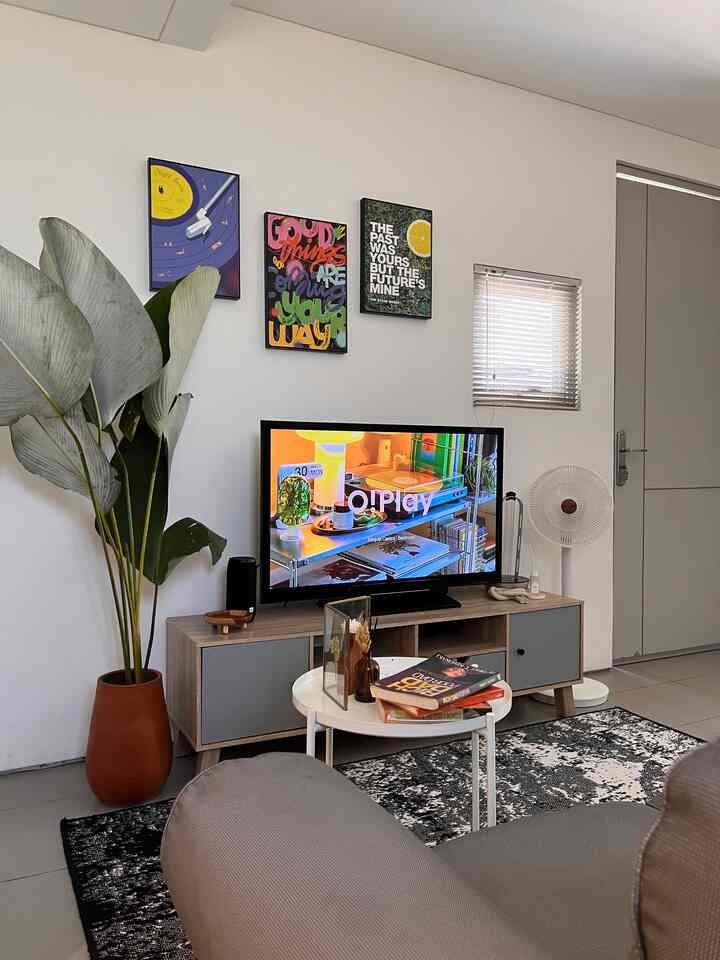 White and light gray toned living room featuring TV stand and plant in a simple modern space