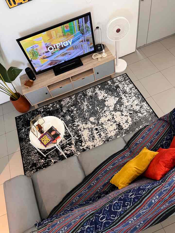 Bright living room with gray sofa and black patterned carpet, wooden TV stand, and white side table creating a cozy atmosphere