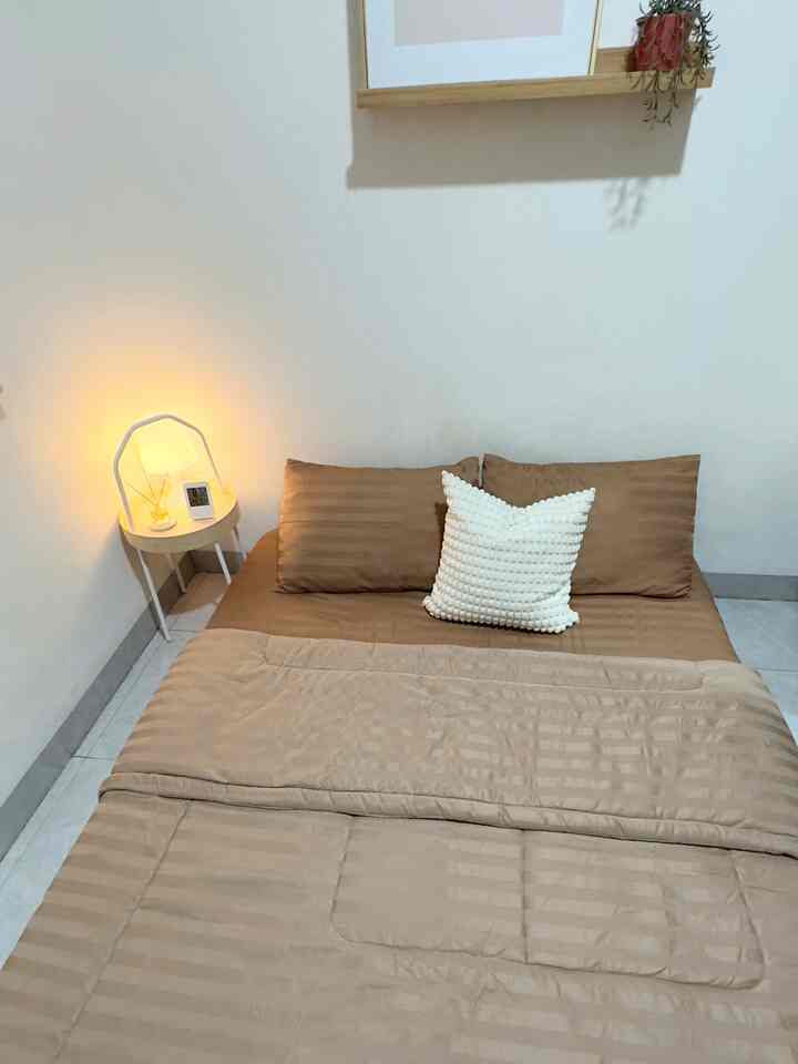 Simple natural small bedroom with brown bedding and white walls, side table with table lamp and diffuser on left