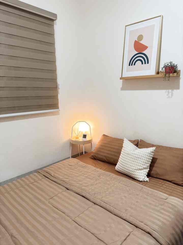 Light brown toned bedroom featuring a neatly made bed with pillows and nightstand lamp creating a cozy atmosphere