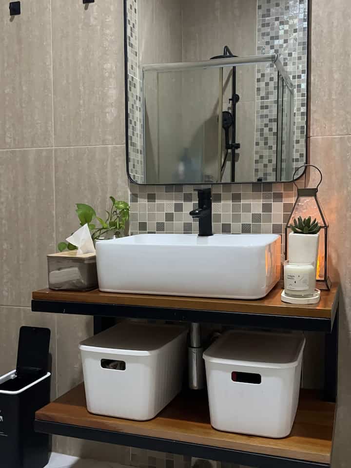 White and brown toned bathroom featuring a sink with storage boxes, plant, and candle creating a cozy atmosphere