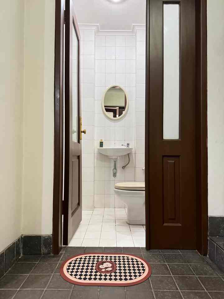 A small, compact powder room with white tiled walls and wood-tone sliding doors, featuring a centrally placed sink and mirror