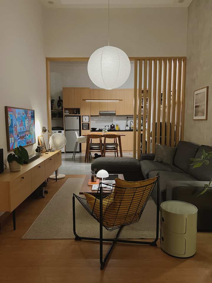 Natural wood-tone and warm-lit living and dining room for a 4-person household, featuring gray sectional sofa and yellow-cushioned armchair in a cozy atmosphere