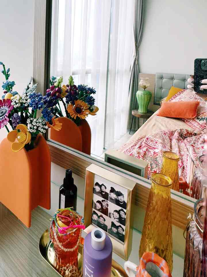 A warm and cozy bedroom in dominant orange and beige tones featuring a flower vase, framed photos, and a large mirror