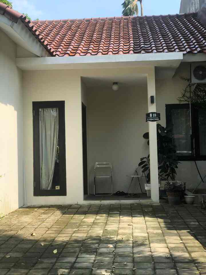 Beige exterior walls and red tiled roof frame a small entrance area of a house with paving block floor and simple furnishings