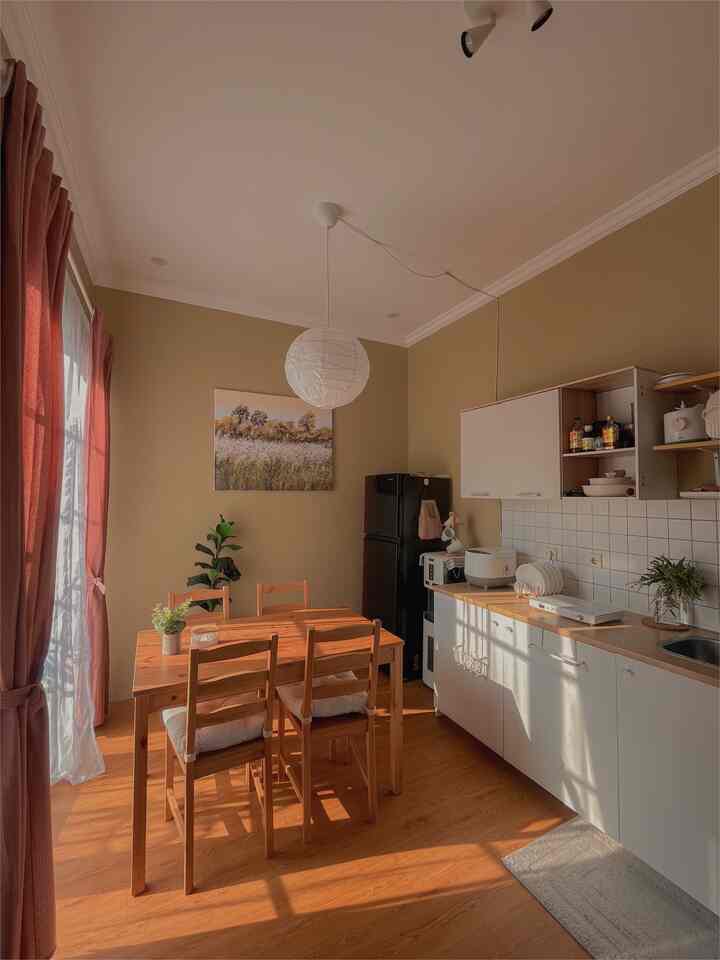 Beige toned walls and wood-tone dining table featured in dining room and kitchen space with natural light creating warm, cozy atmosphere