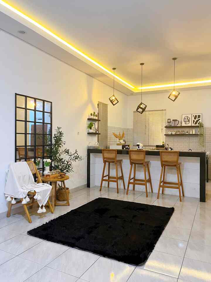 Monotone cafe-style living area with white walls and light gray floors, featuring wood-tone bar stools and a large black shaggy rug creating a cozy atmosphere