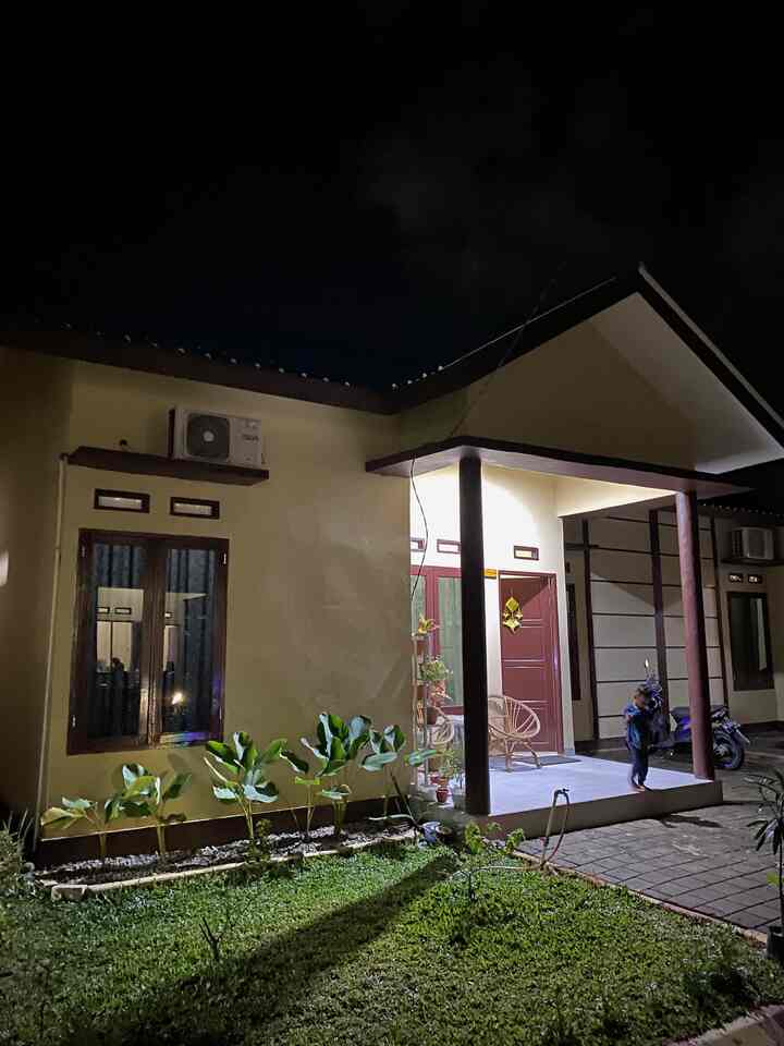 Simple house facade in beige and light brown tones, featuring outdoor garden and entrance porch at night
