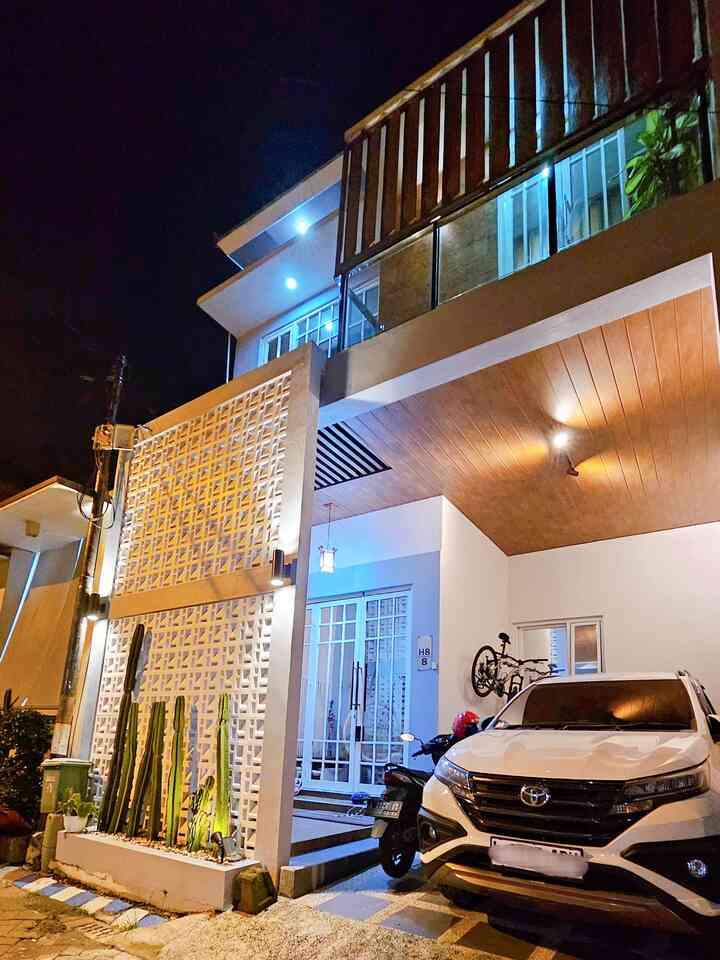 Modern minimalistic house facade featuring warm wood-tone ceiling, white walls, roster screen, entrance, and a parked car at the driveway
