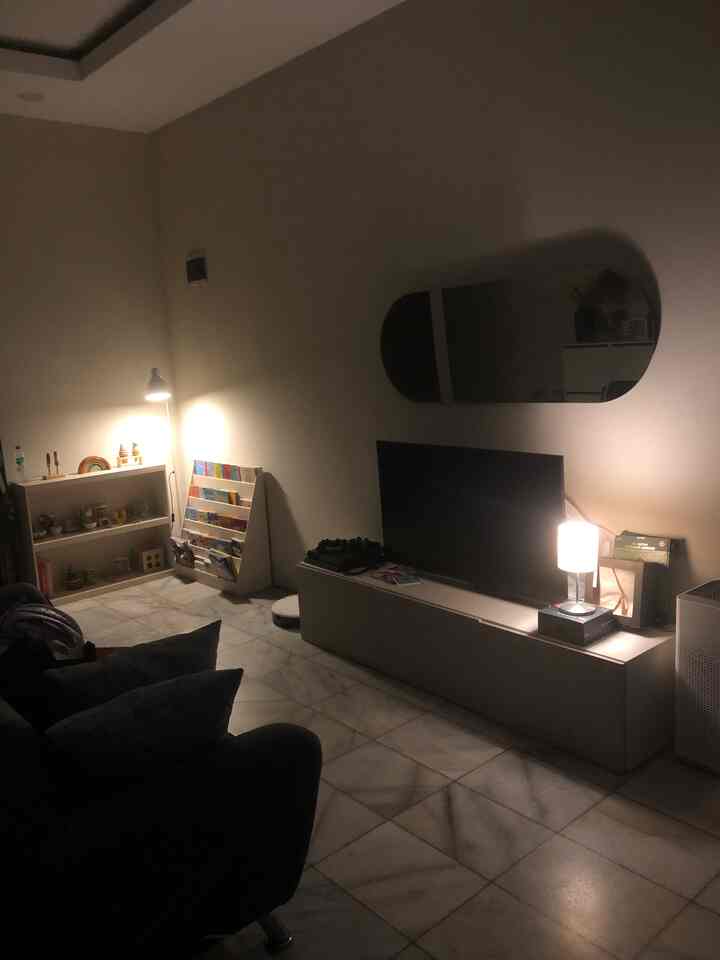 Cozy small living room with warm lighting and white walls, featuring a TV stand, sofa, and children's bookshelf