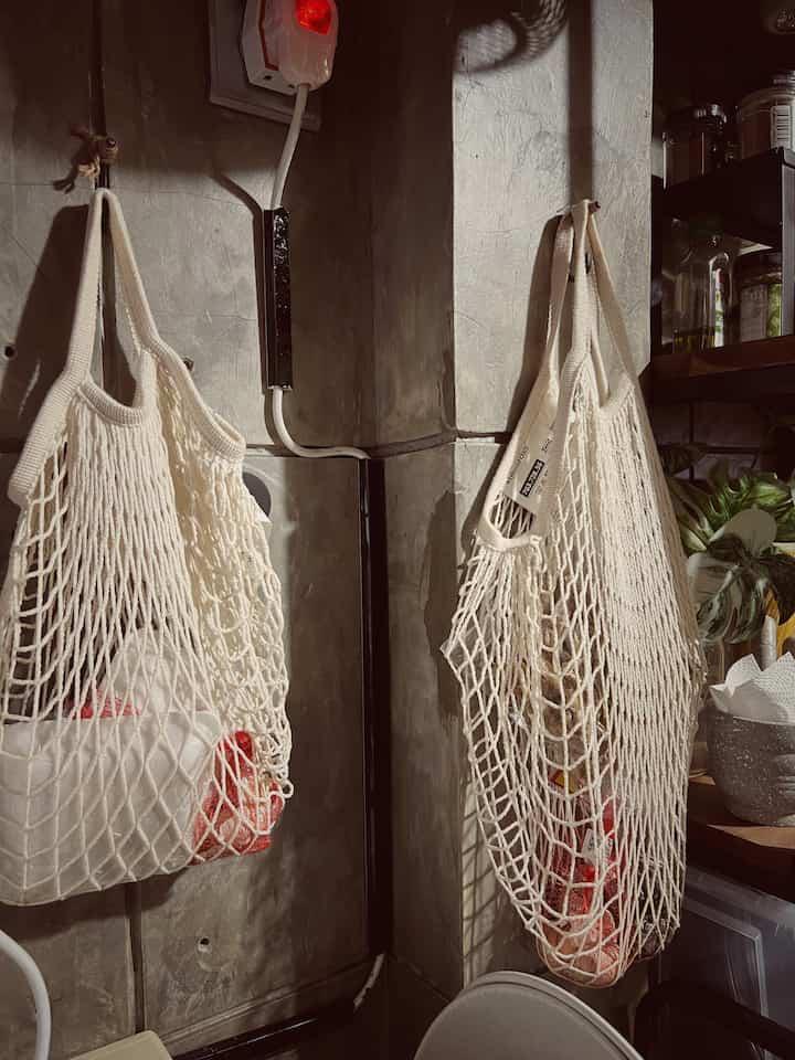 Natural color tone kitchen corner featuring hanging mesh bags and kitchen storage creating a cozy atmosphere