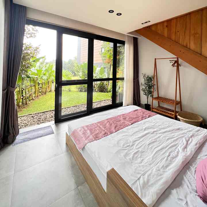 Natural and white toned bedroom with wood tone furniture, large glass windows showcasing natural light and garden view, creating a peaceful atmosphere