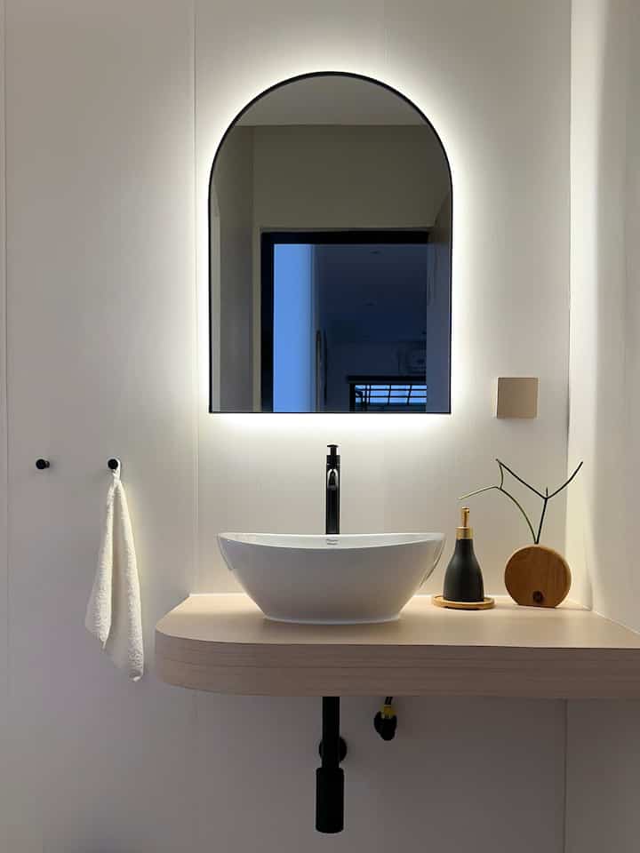 White and wood tone Scandinavian-style powder room featuring sleek black accessories and a unique washbasin