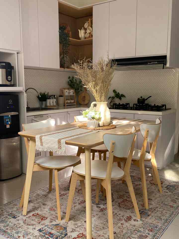 Bright wood-tone and white kitchen space featuring a dining table for four and a patterned carpet, creating a natural atmosphere