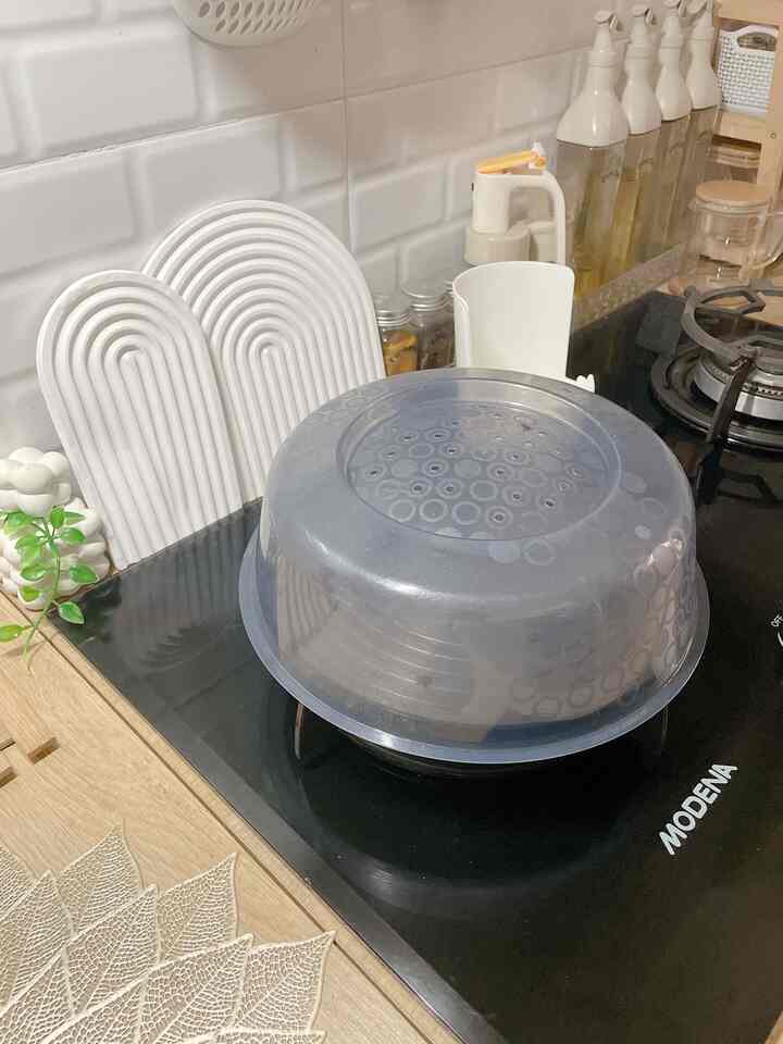Kitchen space featuring white tiled wall and black gas stove, with a transparent plastic tray placed on the dining surface