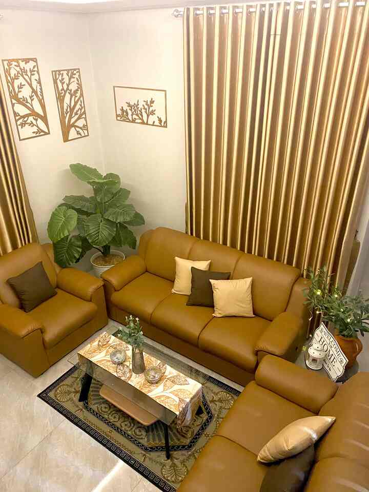 Brown and beige toned living room featuring a leather sofa set, curtains, plants, and wall decor arranged for a cozy atmosphere