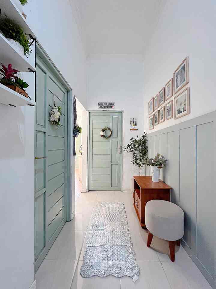 Bright white and wood tone entrance hallway featuring a cream stool and picture frames on the right, creating a cozy and clean atmosphere