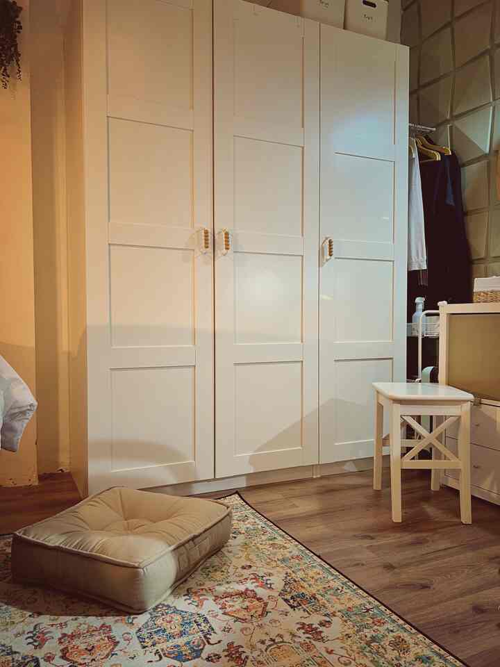 Natural and white-toned small bedroom featuring large white wardrobe and beige floor cushion creating cozy atmosphere