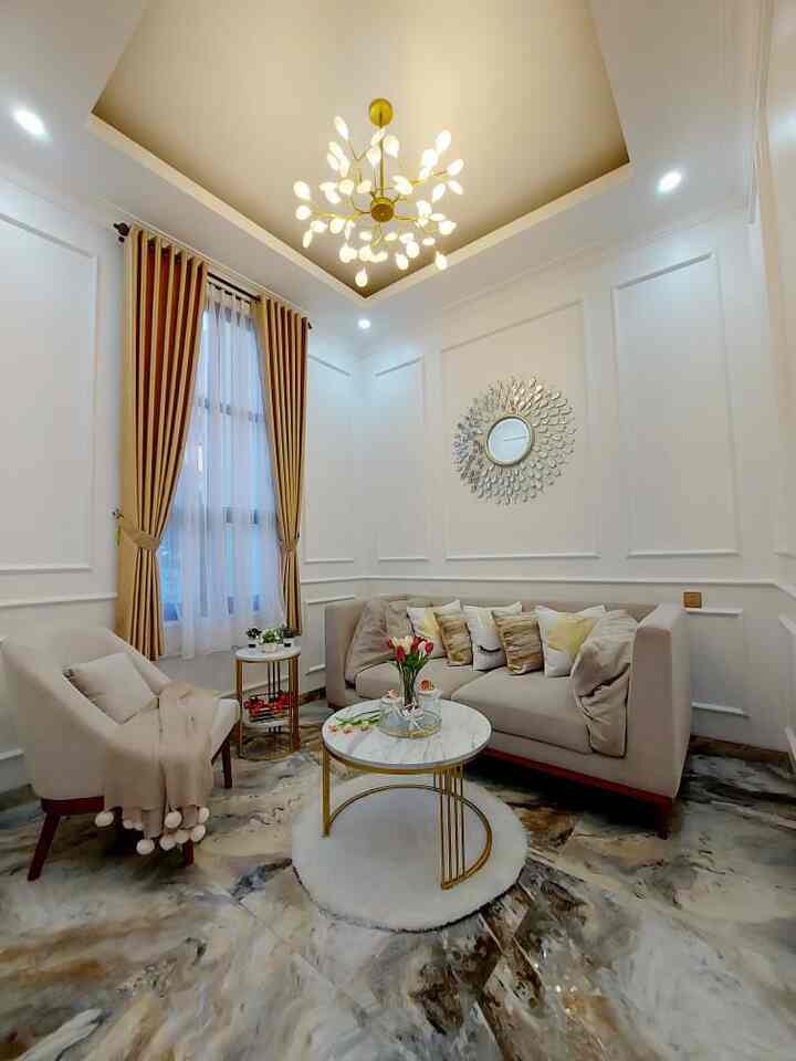 A white and beige toned living room featuring modern sofa and armchair, gold chandelier, and marble coffee table creating a cozy atmosphere