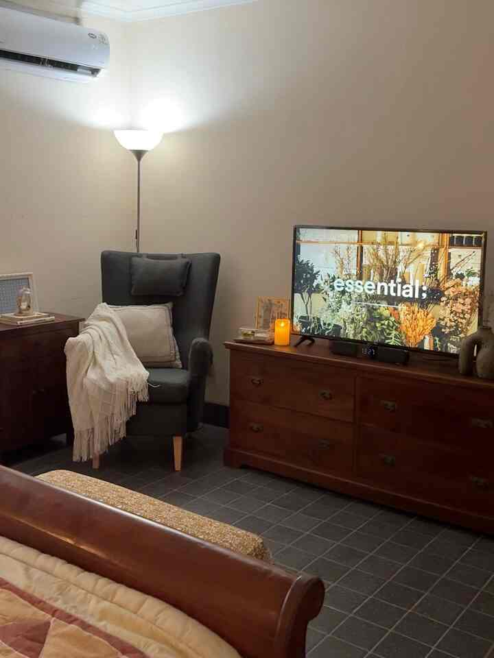 Warm brown and dark gray toned bedroom featuring wooden furniture, armchair, and TV stand creating a cozy atmosphere