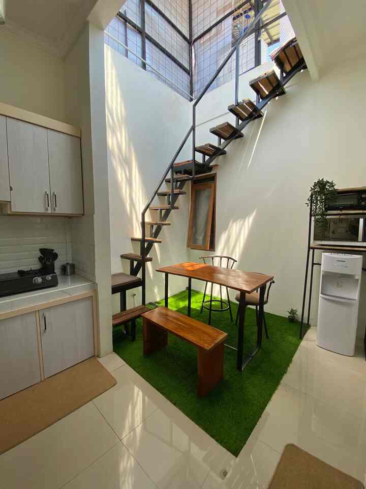 Modern kitchen and dining area with white walls and green synthetic grass carpet, featuring wooden table, bench near indoor staircase
