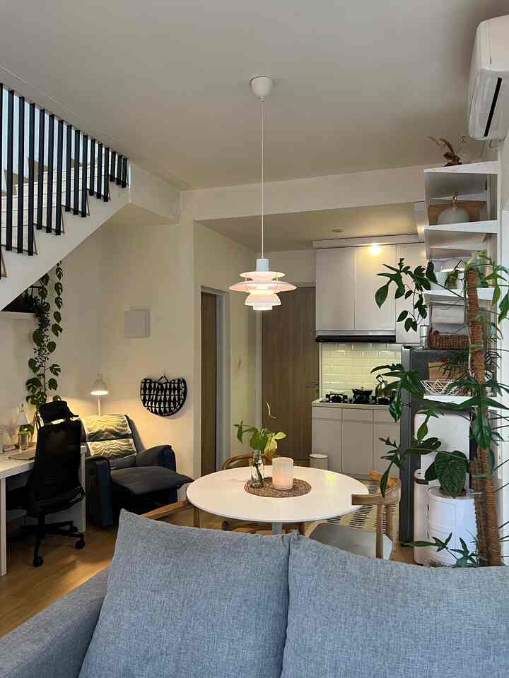 White and gray toned living and dining area featuring a gray sofa, round dining table, and pendant light creating a cozy, clean atmosphere