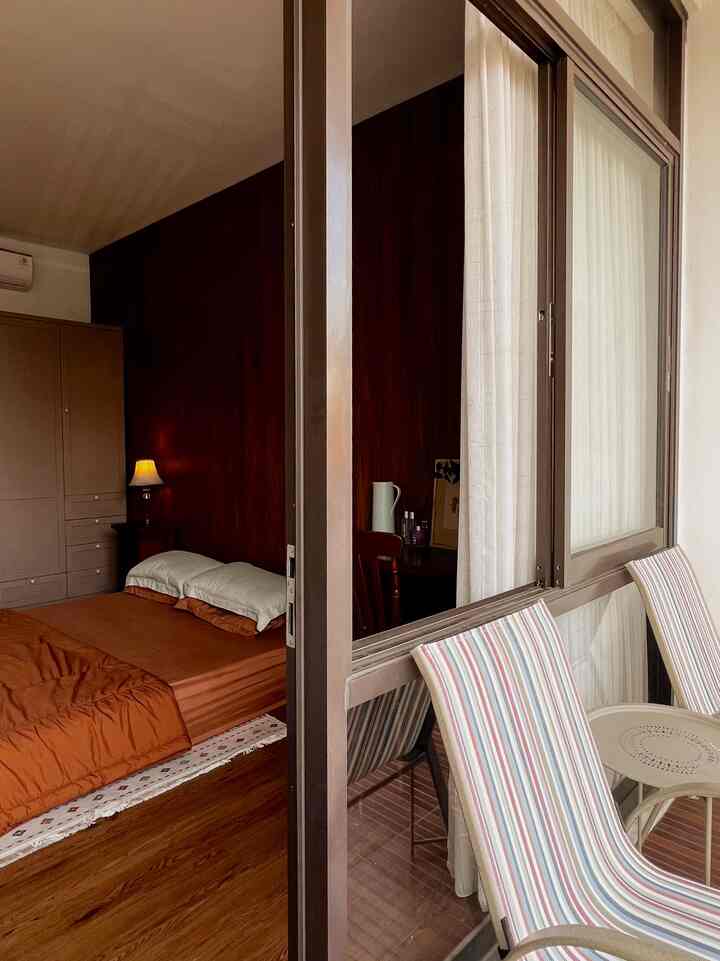 Warm brown tone bedroom and balcony featuring bed and striped outdoor chairs, creating cozy atmosphere