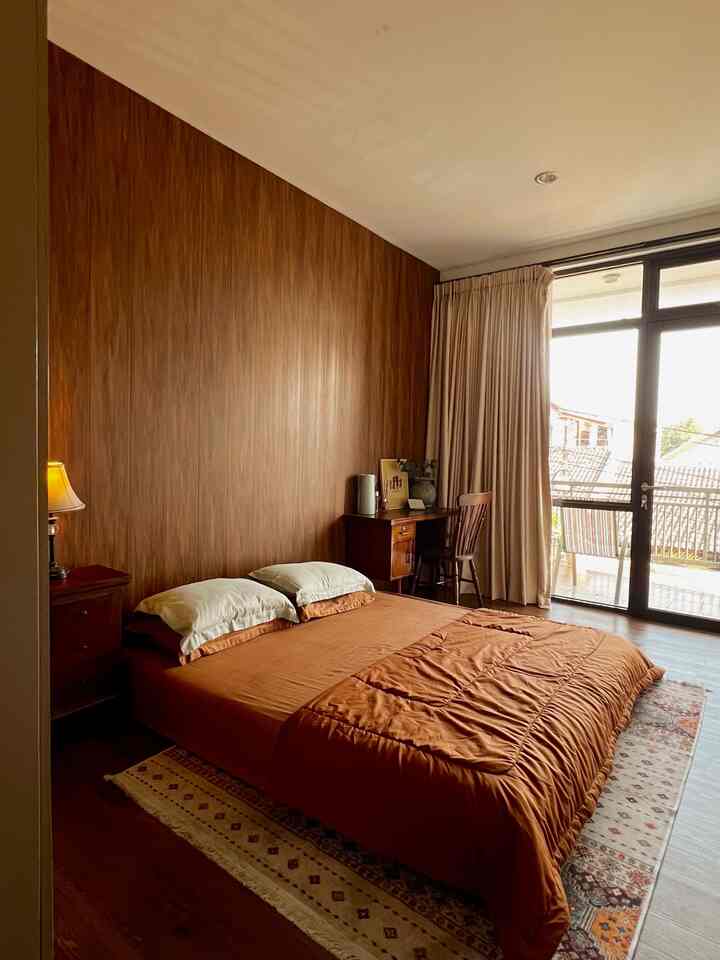 Warm wood-tone bedroom featuring brown bedding, a window with curtains, and wooden desk creating a cozy atmosphere