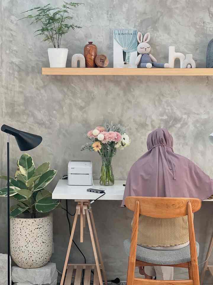 Natural wood furniture and gray-toned wall in a home office space featuring flowers and plants creating a cozy work environment